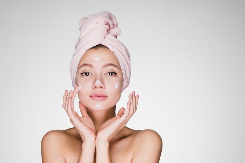 Decorative image of a girl with a towel wrapped around her head and dollops of cream on her face for the post BB Cream Vs CC Cream And Foundation Vs Tinted Moisturisers: What's the Difference?
